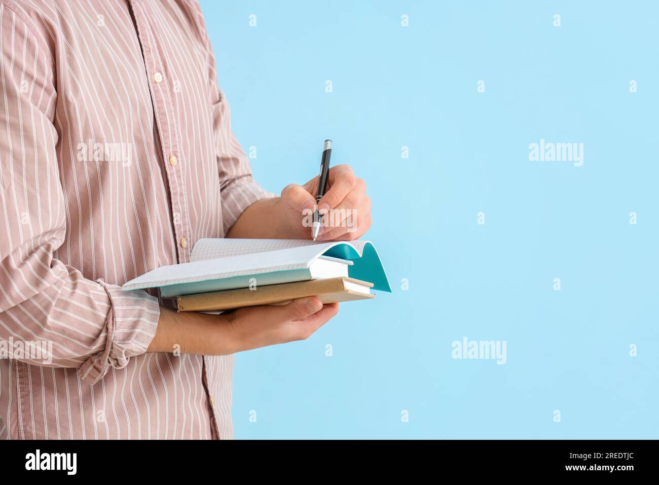 Male student writing in notebook on blue background Stock Photo