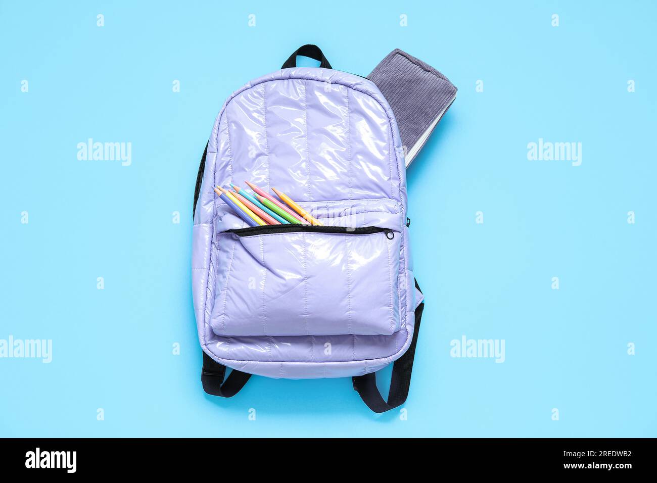 Lilac school backpack with stationery on blue background Stock Photo
