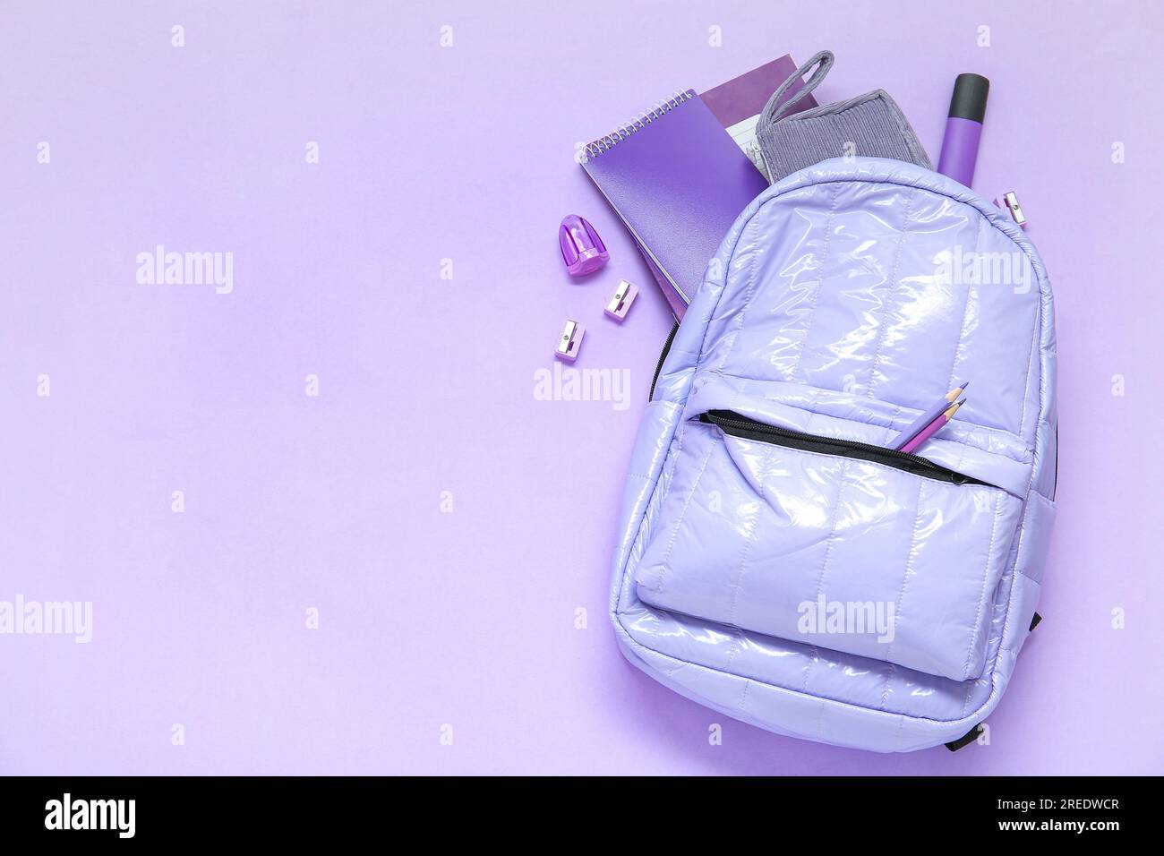 Lilac school backpack with different stationery on purple background Stock Photo