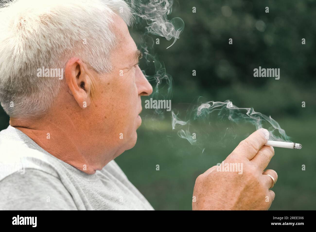 pension cigarette Senior man lighting up a cigarette outdoors against green nature  background. Old thoughtful man smoking, looking aside. Close Up Face.  Relaxed pension Stock Photo