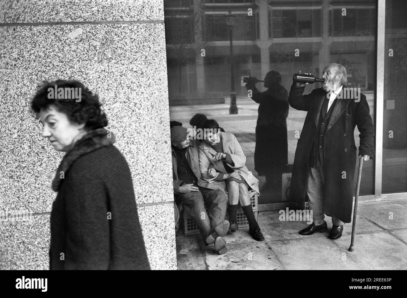 Homeless men 1970s London. An old wino a tramp enjoy a drink from a bottle and his friend chats with female homeless woman. A passer by  avoids the group. Victoria, London 1976 UK HOMER SYKES. Stock Photo