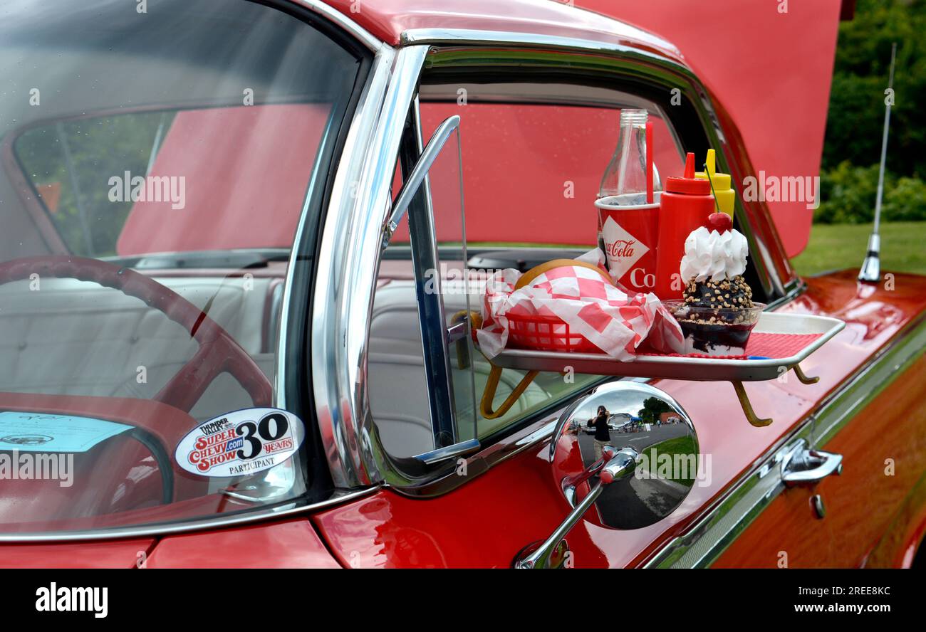A 1950s Chevrolet convertible on display at a car show features a drive-in restaurant window tray with fast food and drinks. Stock Photo