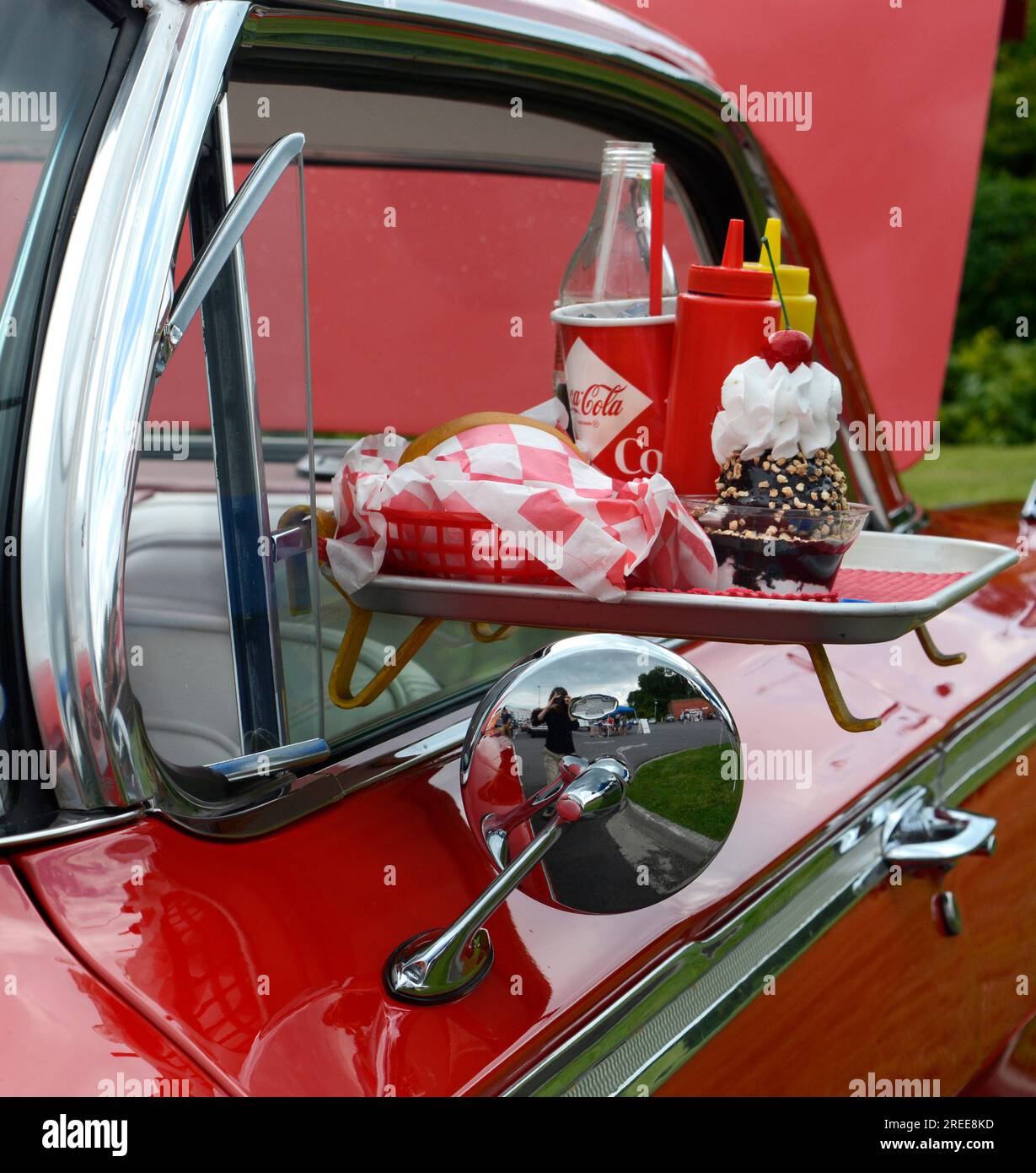 A 1950s Chevrolet convertible on display at a car show features a drive-in restaurant window tray with fast food and drinks. Stock Photo