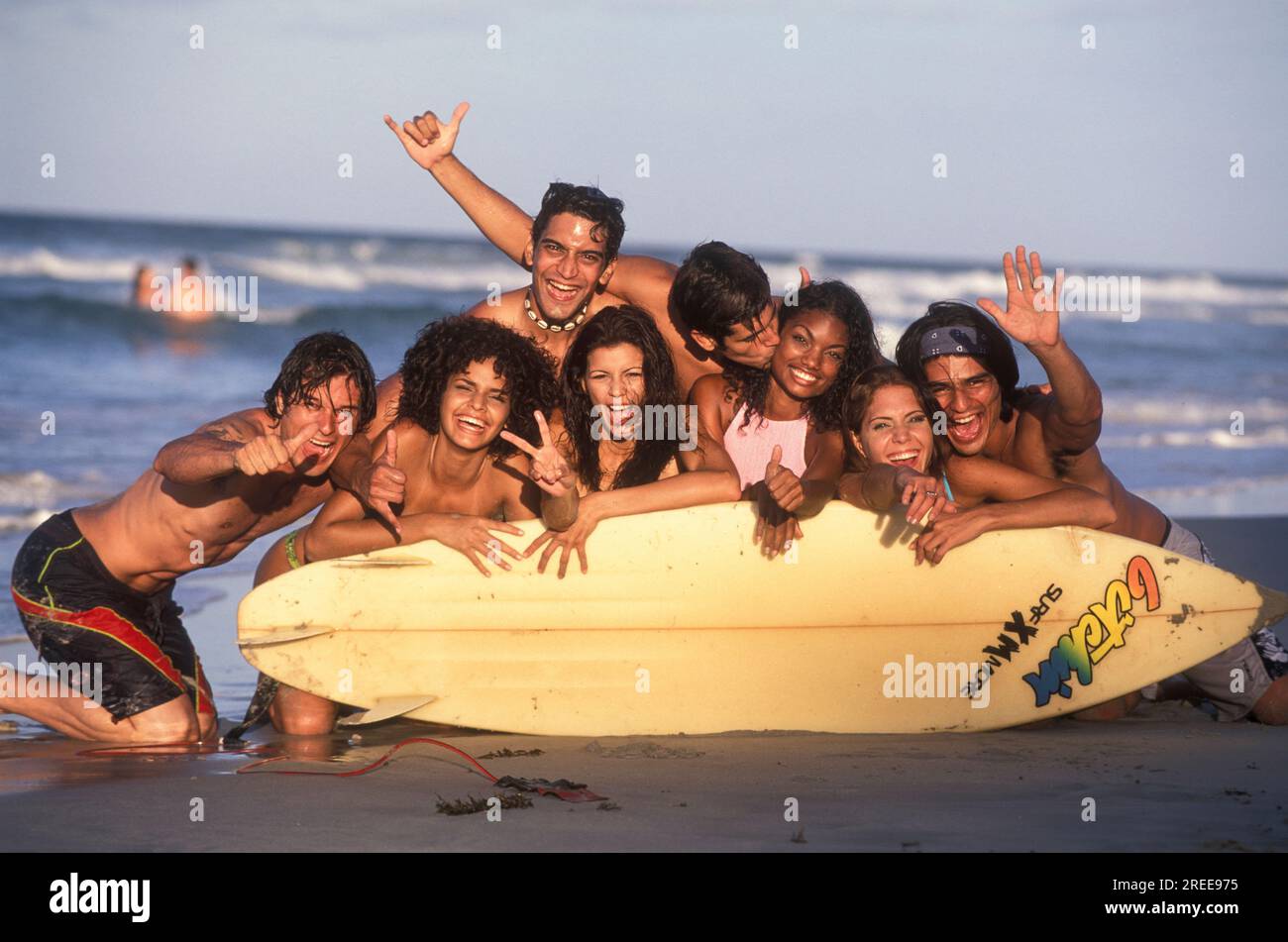 Portrait of a group of young adults behind a surfboard at beach, Margarita Island, Venezuela