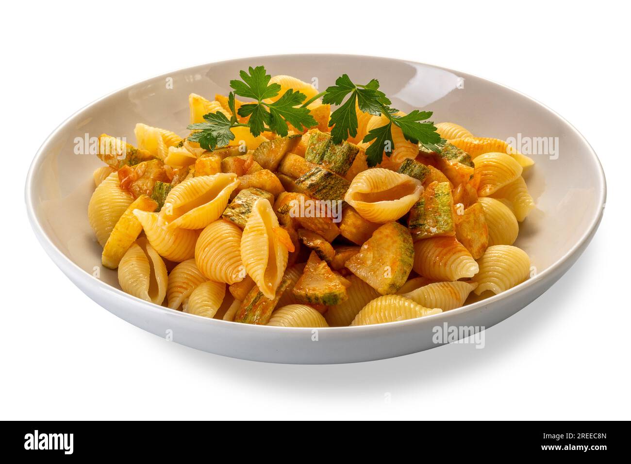 Conchiglie rigate pasta. Macaroni in shape of ridged shell with courgette and tomato sauce with parsley leaves in white dish isolated on white with cl Stock Photo