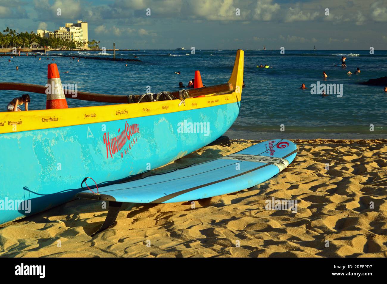 An outrigger canoe and a surf board, two popular modes of transportation in Hawaii, rest on the sand of Waikiki Beach Stock Photo