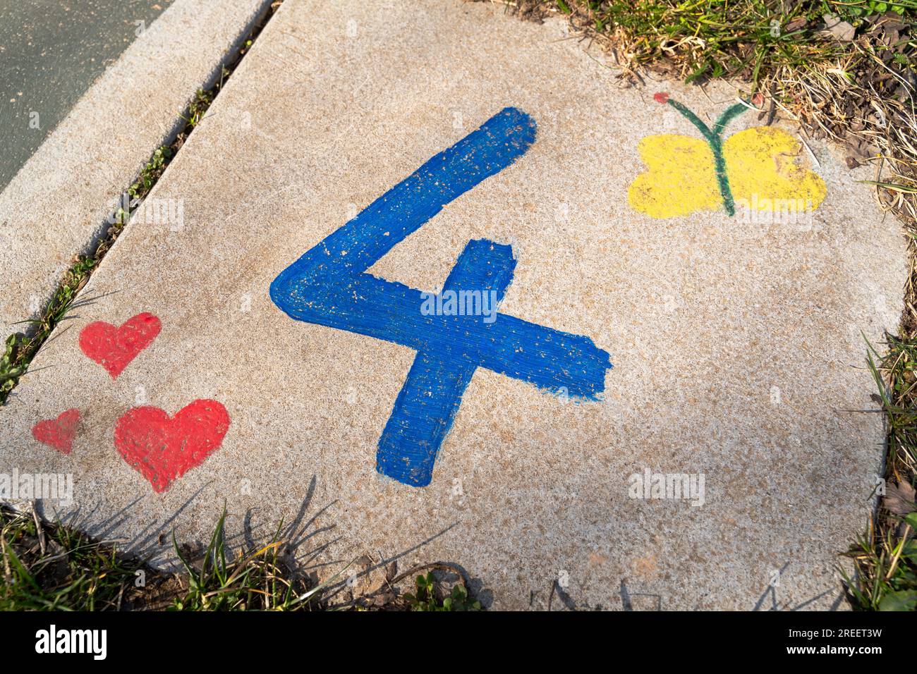Curb painted by children with a blue number 4, red hearts and a yellow butterfly Stock Photo