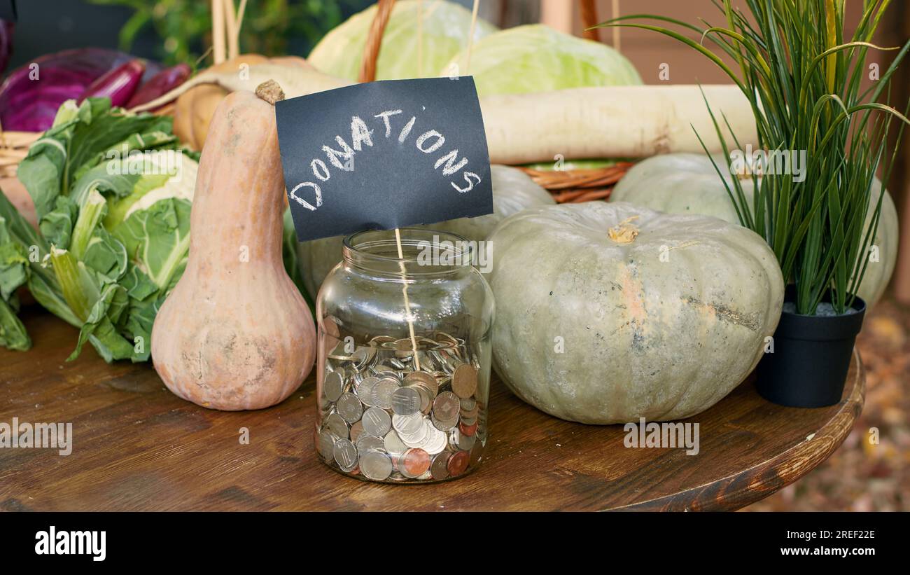 Table with homegrown vegetables and bottles of wine, jar filled with coins for local donations. Greenmarket stall with organic eco lettuce or cabbage, raw pumpkin and zucchini. Close up. Stock Photo