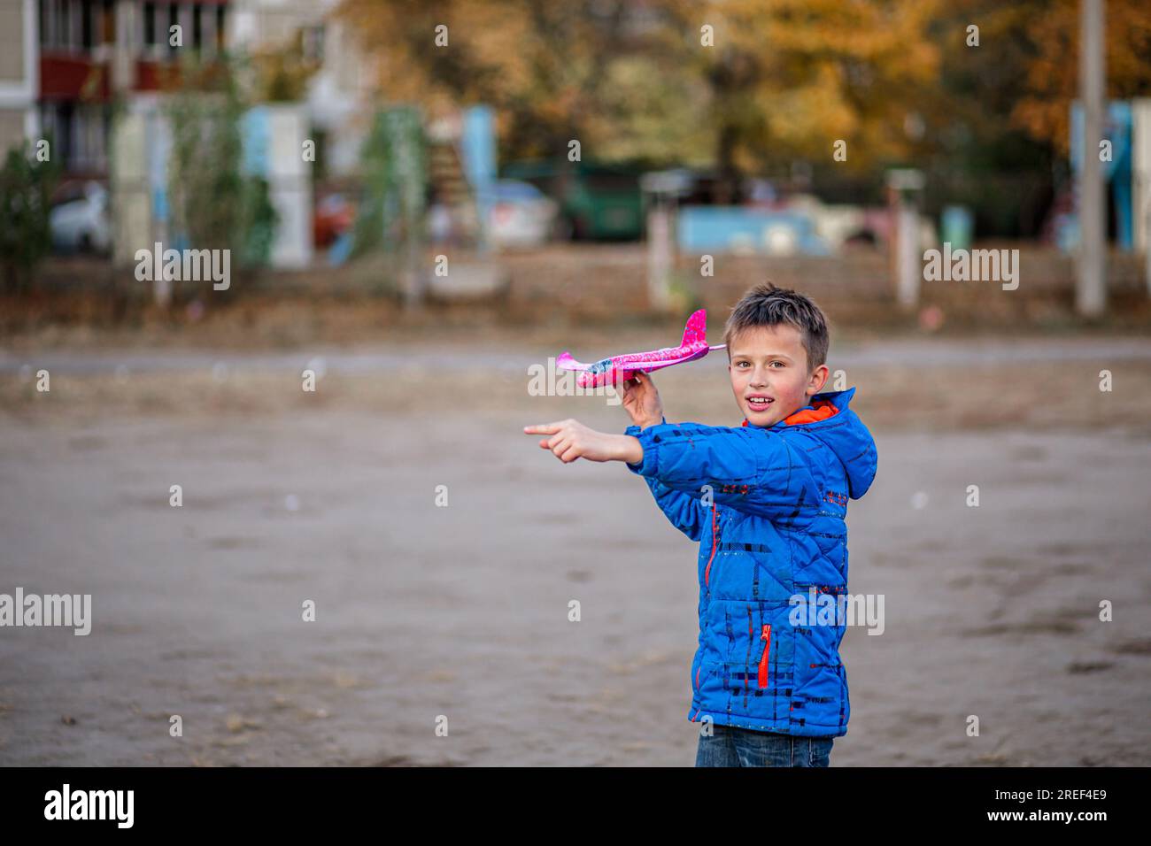 boy joyfully launches his toy plane at the stadium in autumn. Childhood Stock Photo