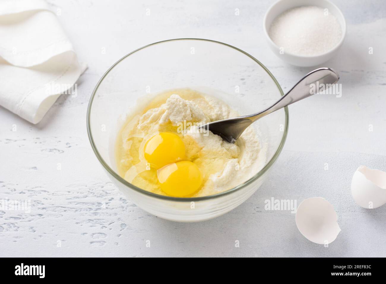 Glass bowl with soaked semolina, eggs and a bowl of sugar. cooking mannik, cake or pie on a light blue background. step by step, cooking step. Stock Photo