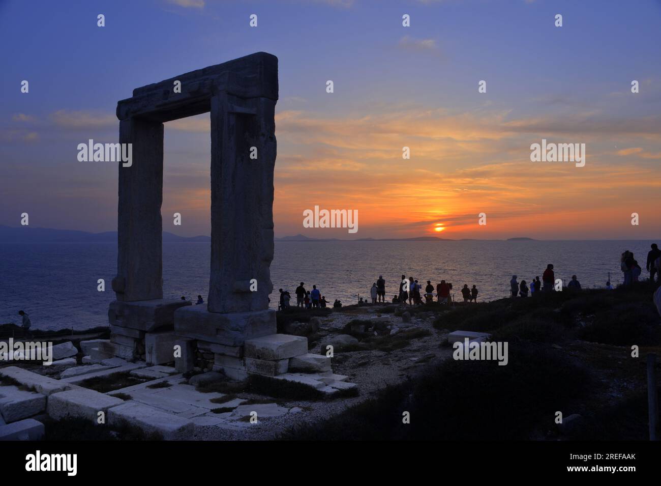 Naxos island, tourists admire the Temple of Apollo entrance at sunset.  Marble doorway standing alone near the sea at sunset. Stock Photo