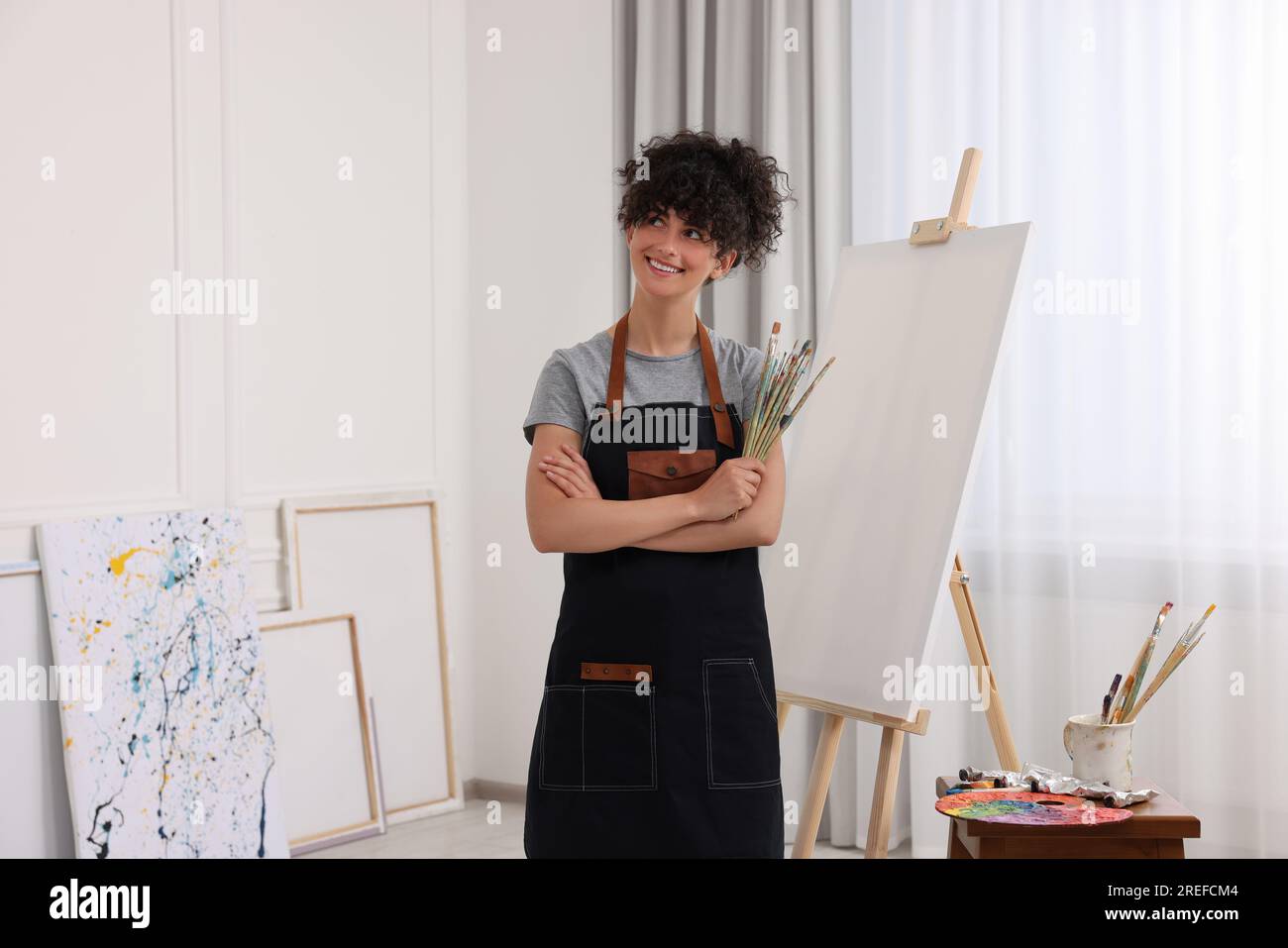 Young woman holding brushes near easel with canvas in studio Stock ...