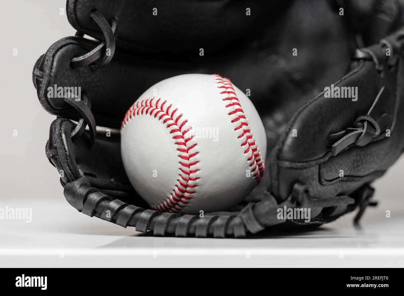Closeup of a white baseball ball with red stitches inside baseball glove Stock Photo