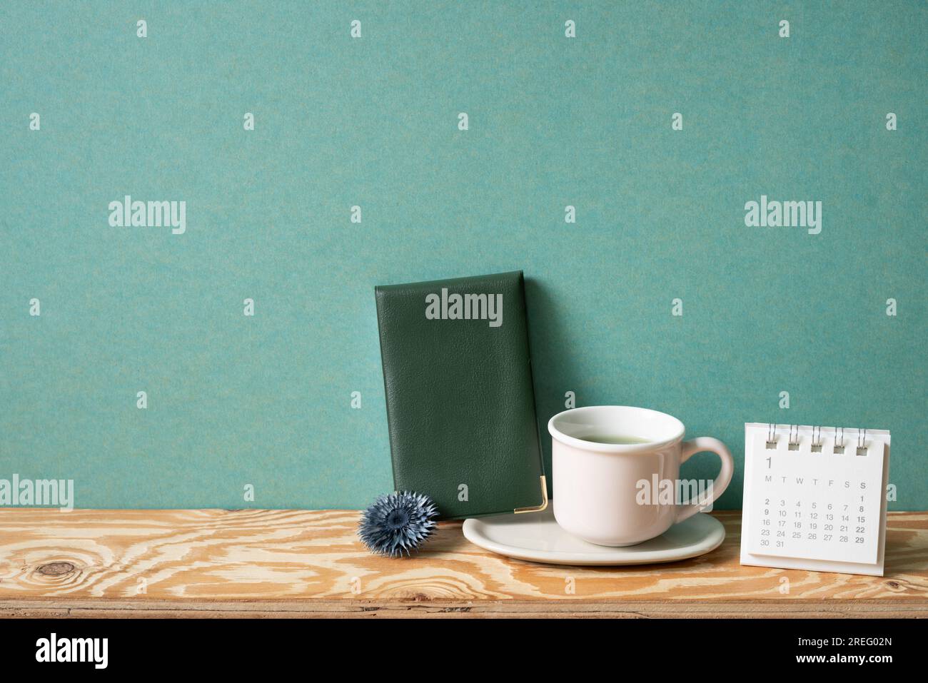 Diary note, cup of tea, calendar on wooden desk. green wall background. copy space Stock Photo