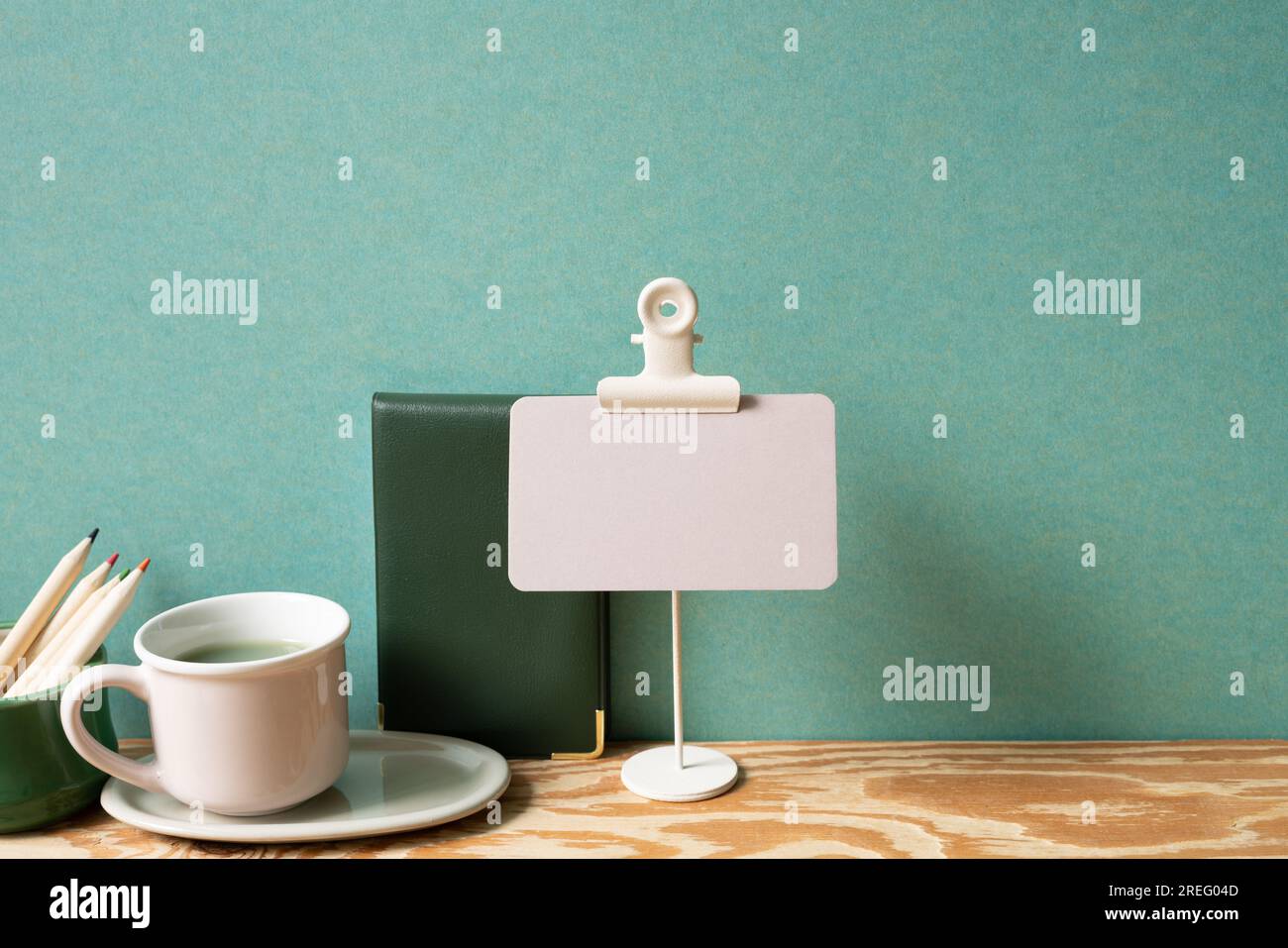 Memo pad, note, cup of tea, colored pencil on wooden desk. green wall background. study and workspace. copy space Stock Photo