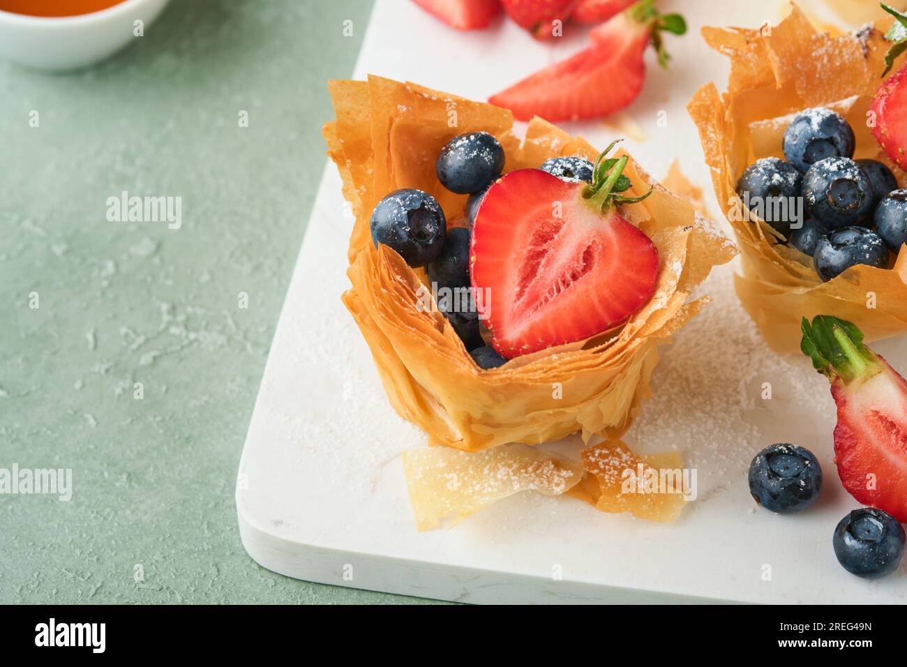 Phyllo or filo pies with fresh berries strawberries and blueberries, cheese filling topped with fresh mint on white plate. Homemade Filo pastry pasket Stock Photo