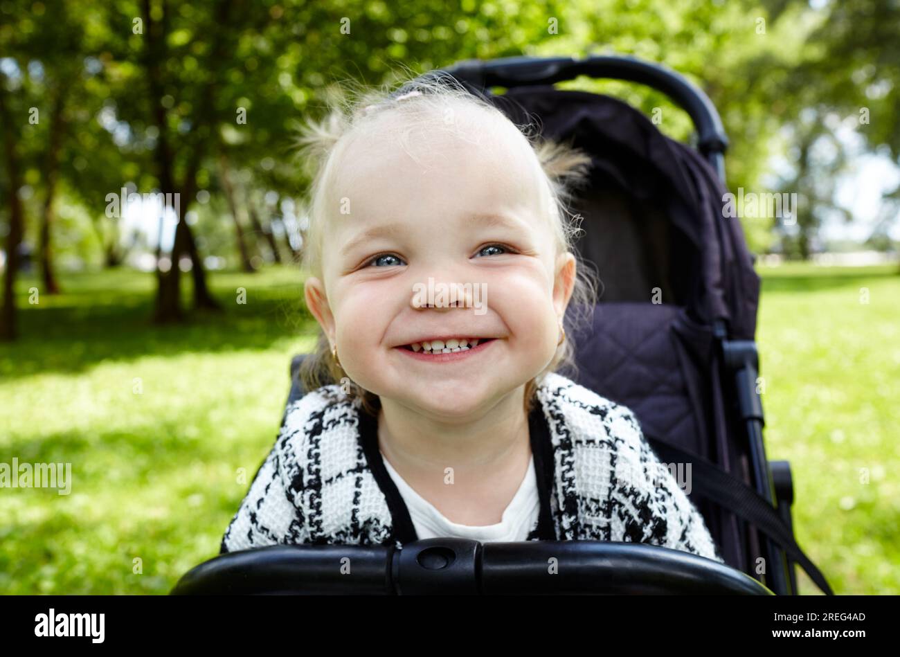 Baby in stroller on a walk in summer park. Adorable little girl sitting