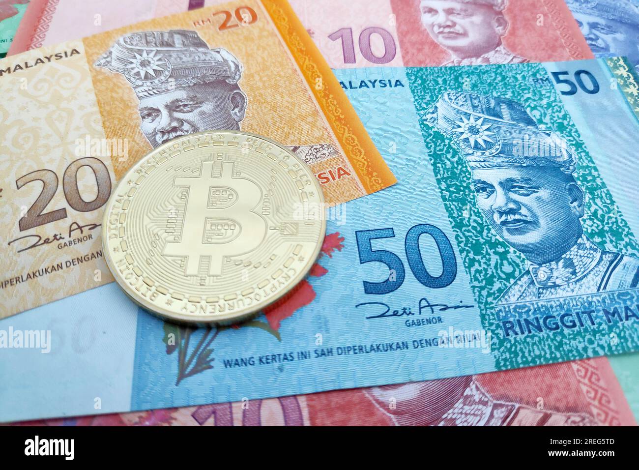 Close-up on a golden Bitcoin coin on top of a stack of Malaysian Ringgit banknotes. Stock Photo