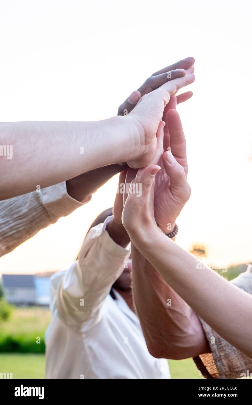 Diverse multiracial cheerful students giving high five greeting each other. Multi-ethnic millennial group of young people slapping palms standing outside. Gesture of celebration, friendship and unity. High quality photo Stock Photo