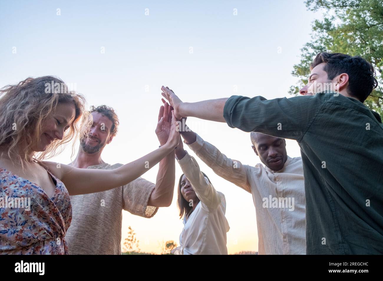 Diverse multiracial cheerful students giving high five greeting each other. Multi-ethnic millennial group of young people slapping palms standing outside. Gesture of celebration, friendship and unity. High quality photo Stock Photo
