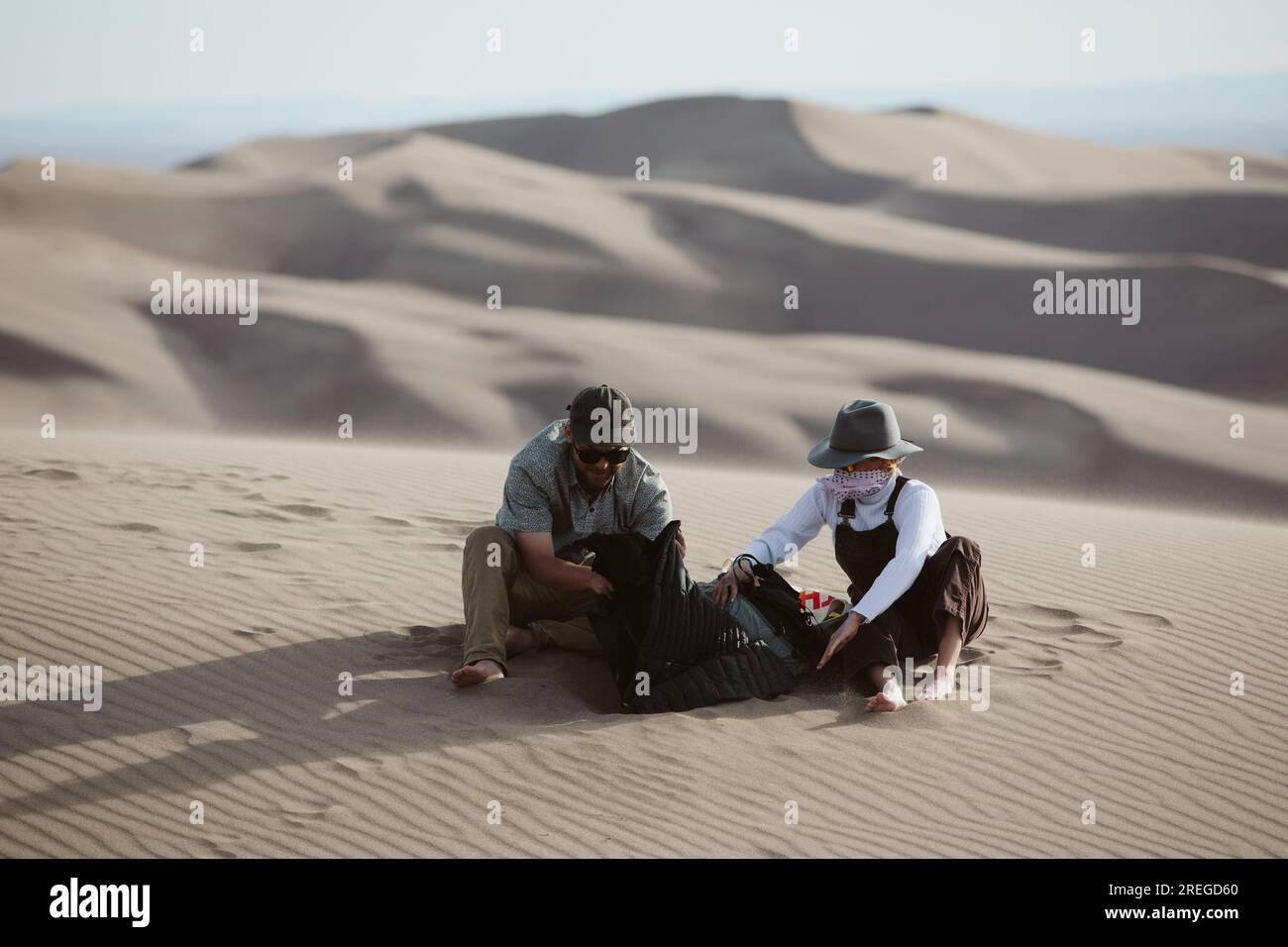 two adventurers take shelter from the whipping wind of the sand dunes Stock Photo