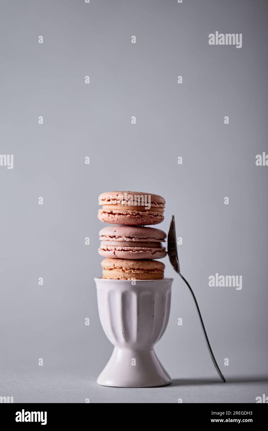 Macarons stacked in a egg cup, fork on the side on gray background Stock Photo