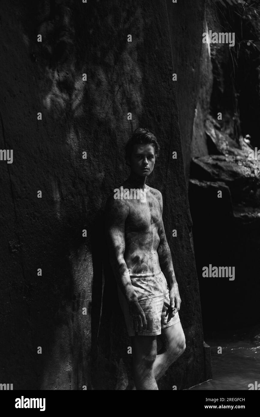 Young tattooed man in tropical jungle, rays of light. Stock Photo