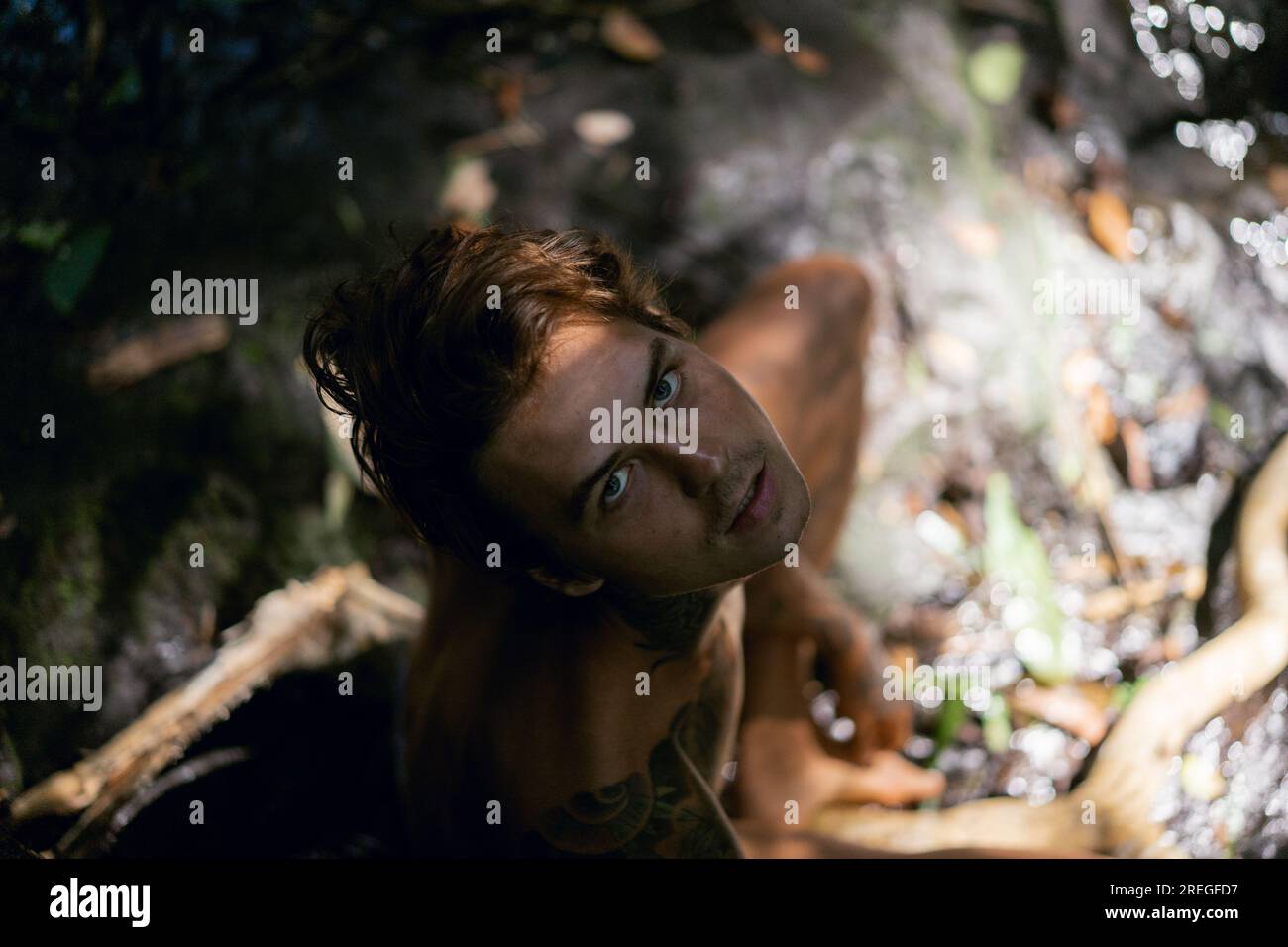 Young tattooed man in tropical jungle, rays of light. Stock Photo