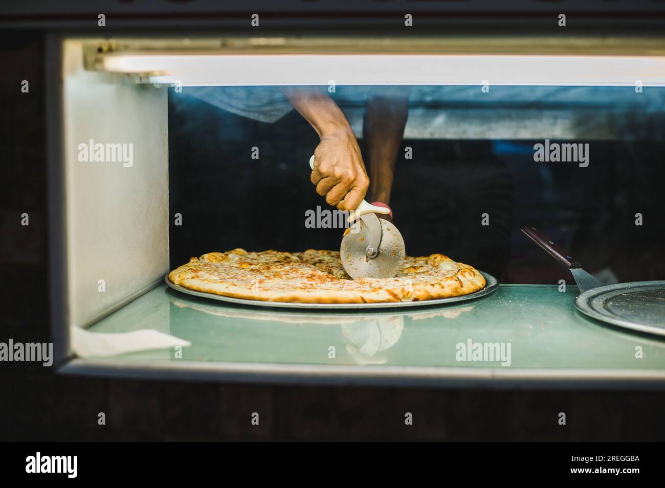 Multicultural hand slices pizza in a NYC 99 cent pizza shop Stock Photo