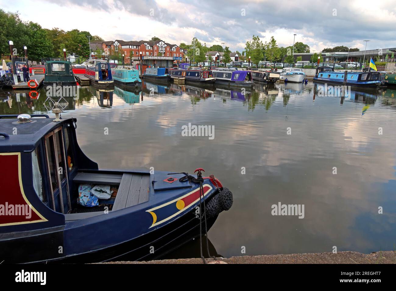 Canal boat in the foreground at Northwich Quay Marina with moored narrowboats and reflections on calm water, Northwich, Cheshire, England, UK CW9 Stock Photo