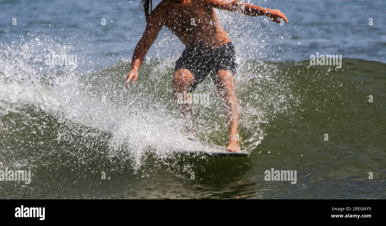 A man is surfing while standing on the front of his surfboard with water splashing all over. Stock Photo