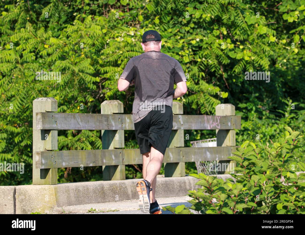 Rear view of a very sweaty man running over the fishing bridge in Southards Pond Park on a hot summer morning. Stock Photo