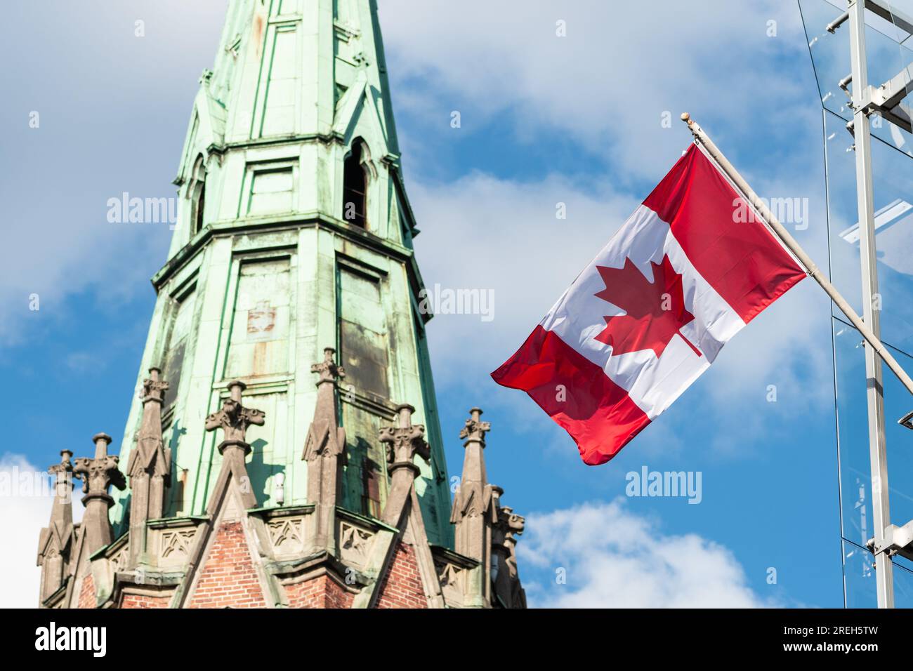 Flag of Canada waiving in the sun with blue sky and church tower on the background on the top of the building of Canadian embassy in Riga, Latvia Stock Photo