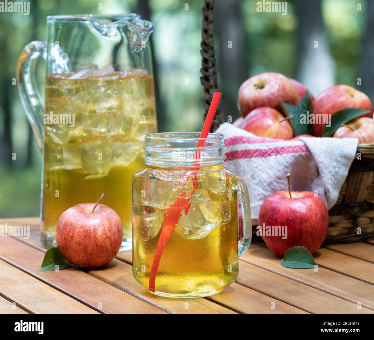 Apple juice in glass jar and pitcher with fressh red apples outdoors on wooden patio table and nature background Stock Photo
