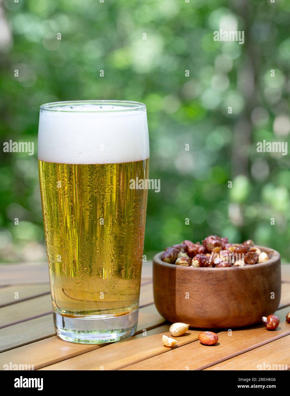 Glass of beer and bowl of nuts outdoors on wooden patio table with nature background Stock Photo