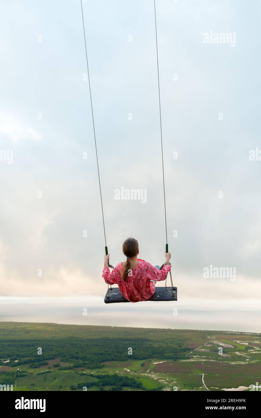 Little girl is on a swing under cloudy sky. Montana Redonda mountain top, Dominican Republic. Vertical photo Stock Photo