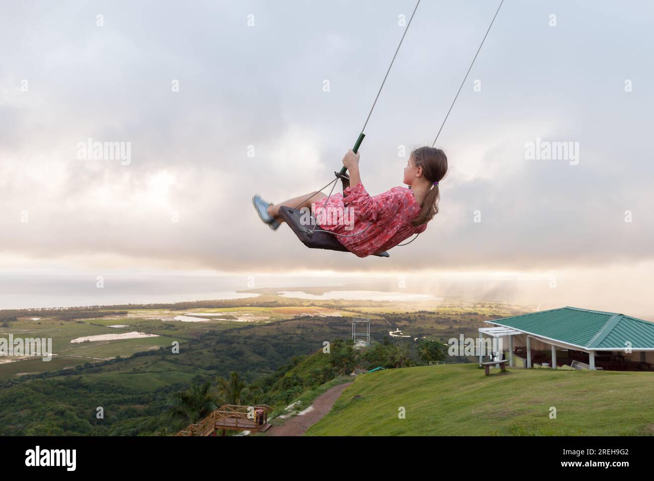 Little girl is on a swing under cloudy sky. Montana Redonda, Dominican Republic Stock Photo