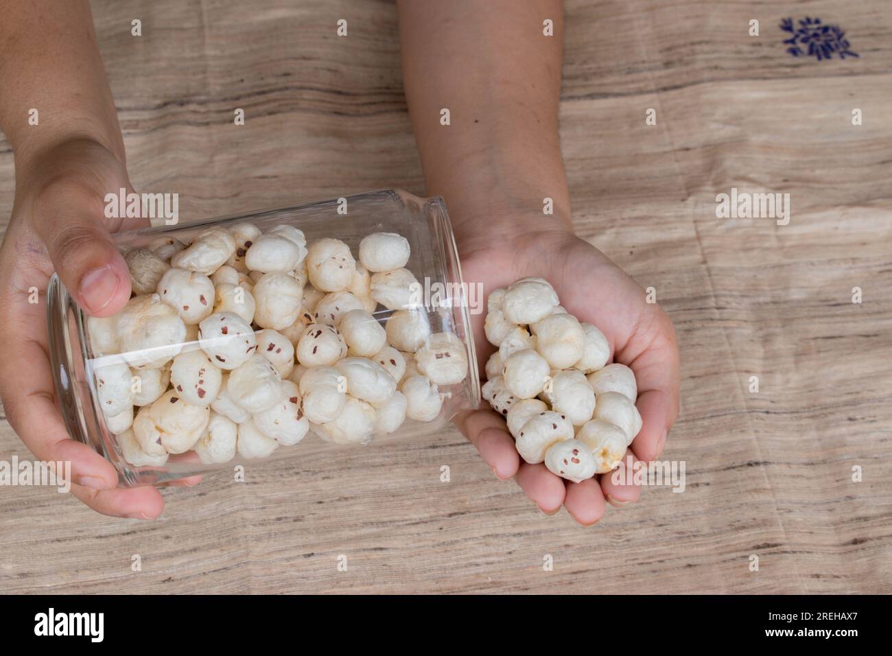 Makhana or foxnut in hand holding glass jar with brown background . copy space Stock Photo