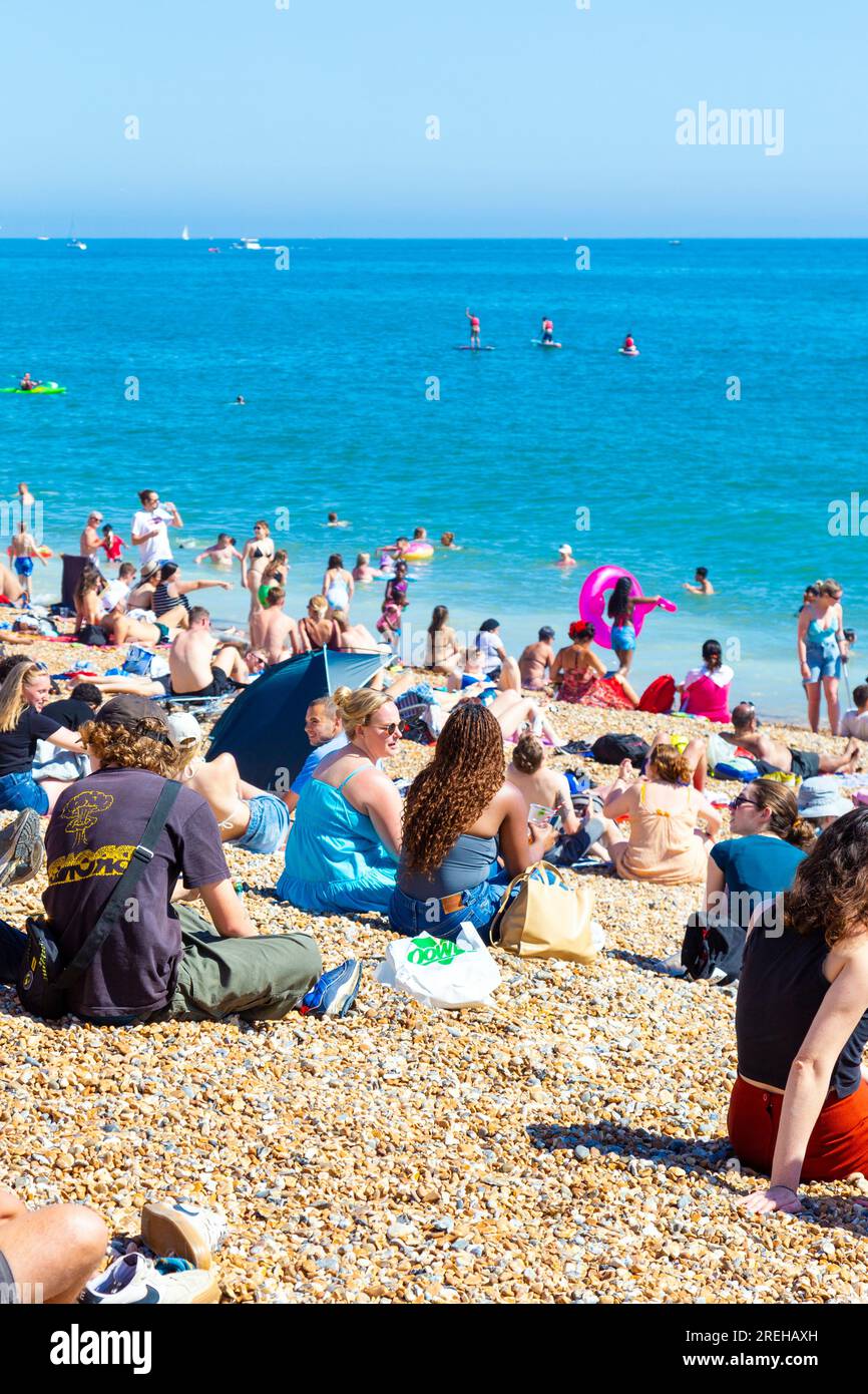 People sitting on the beach on a hot summer day with Brighton Palace Pier in background, Brighton, UK Stock Photo