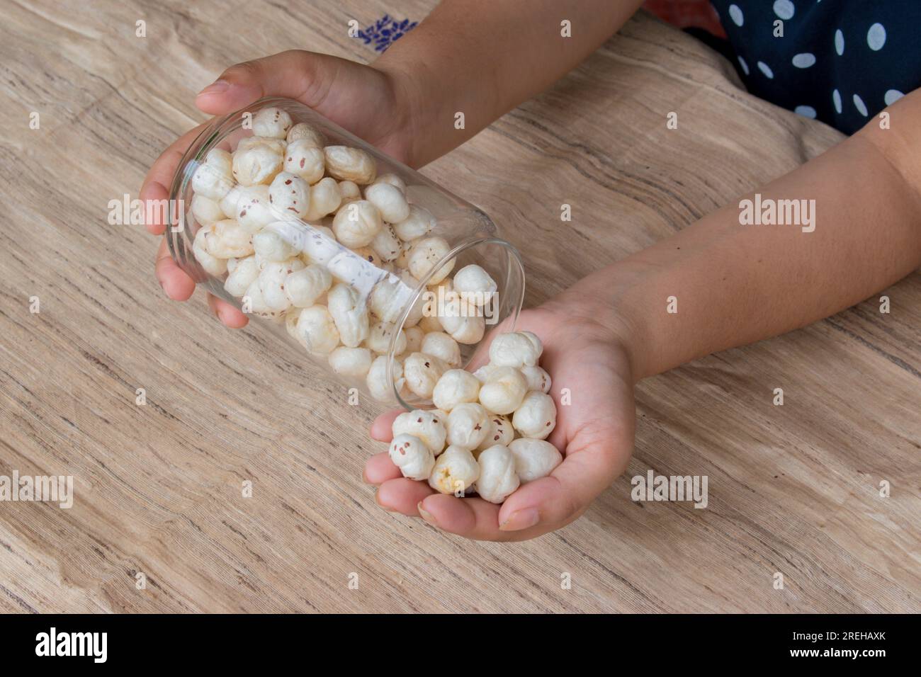 Makhana or foxnut in hand holding glass jar with brown background . copy space Stock Photo