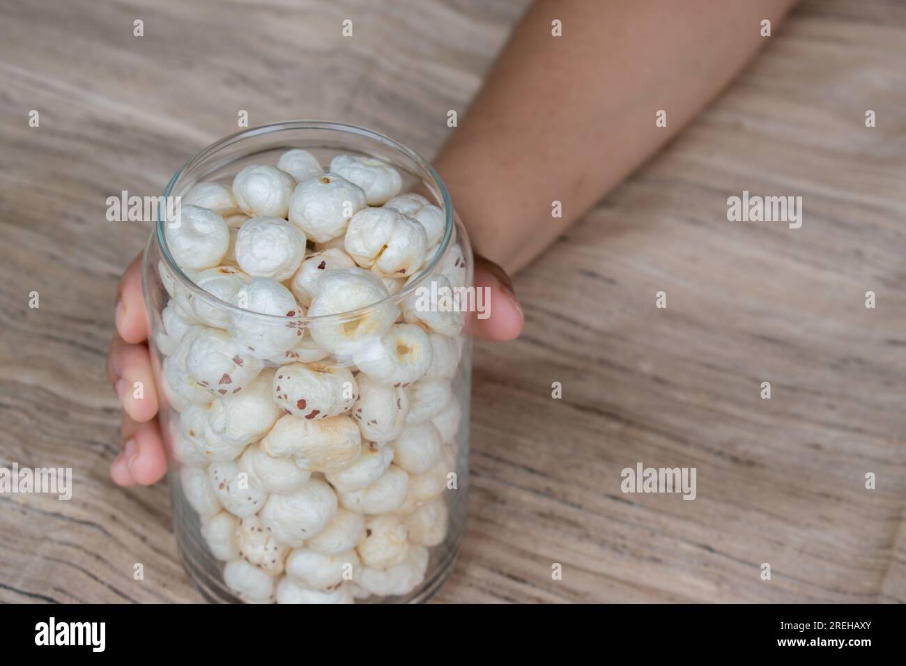 Makhana or foxnut in hand holding glass jar with brown background . Stock Photo