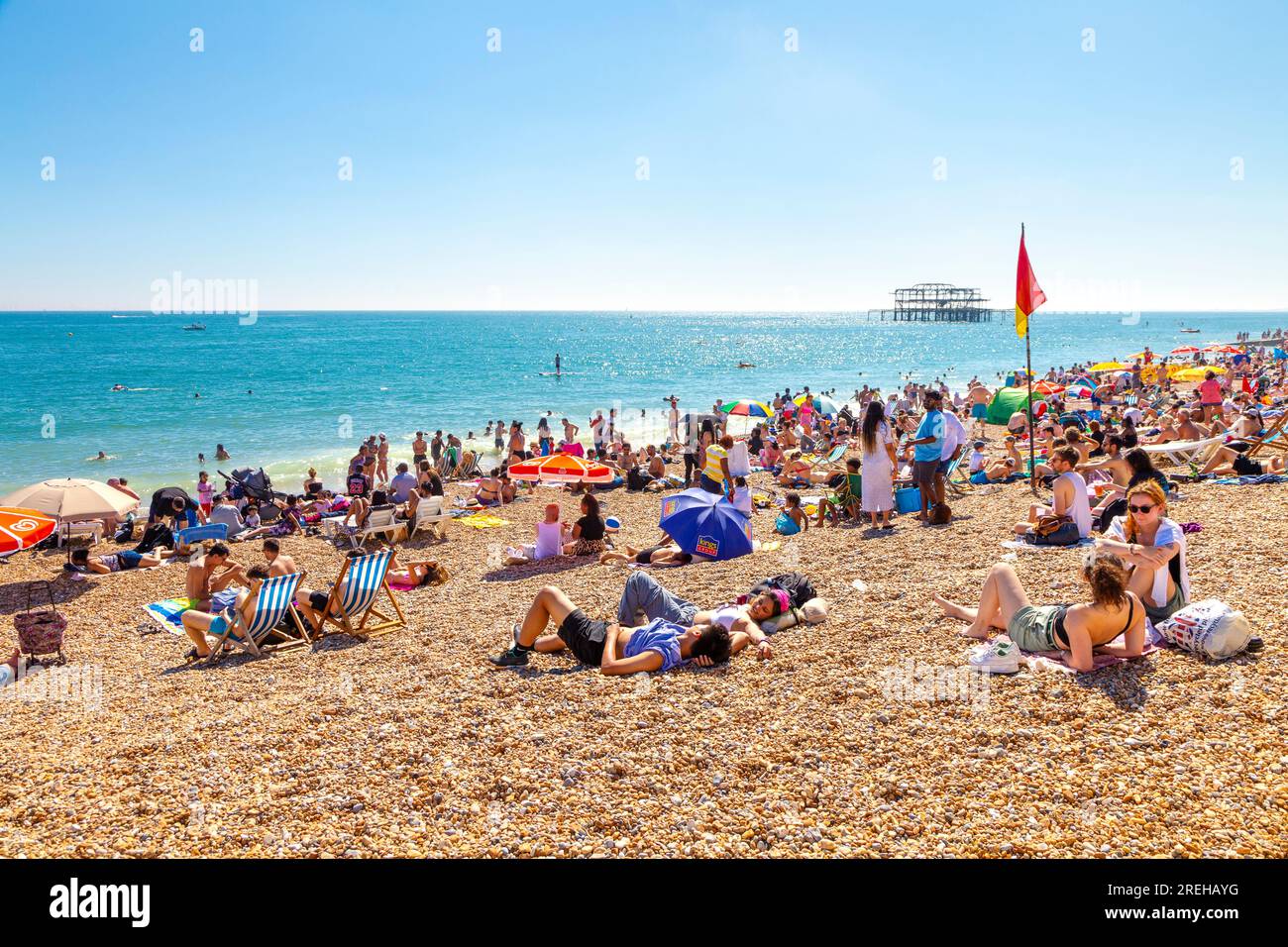 People sitting on the beach on a hot summer day with the burned down West Pier in background, Brighton, UK Stock Photo