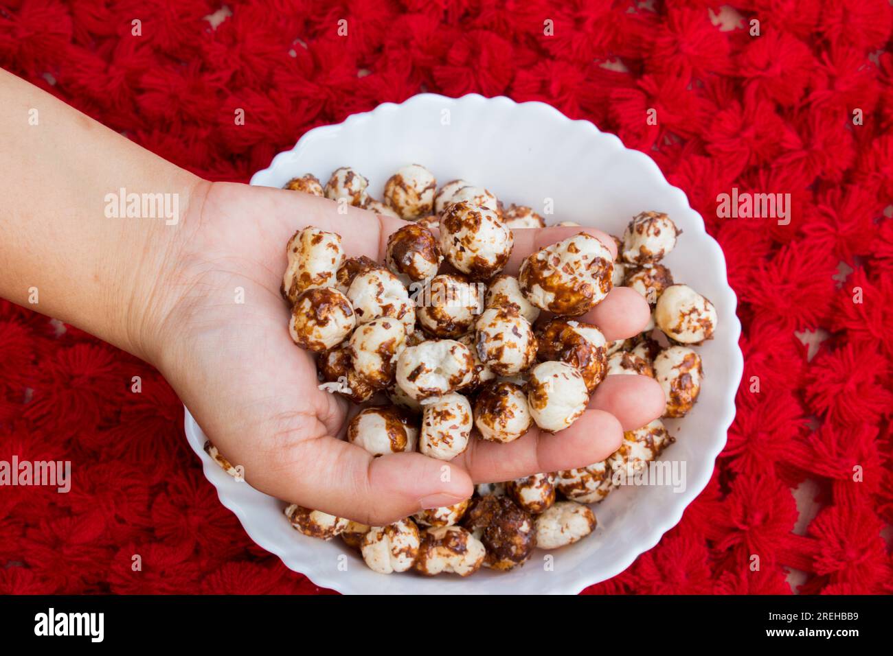 Hand holding healthy Chocolate and jaggery coated makhana in beautiful red background. copyspace Stock Photo