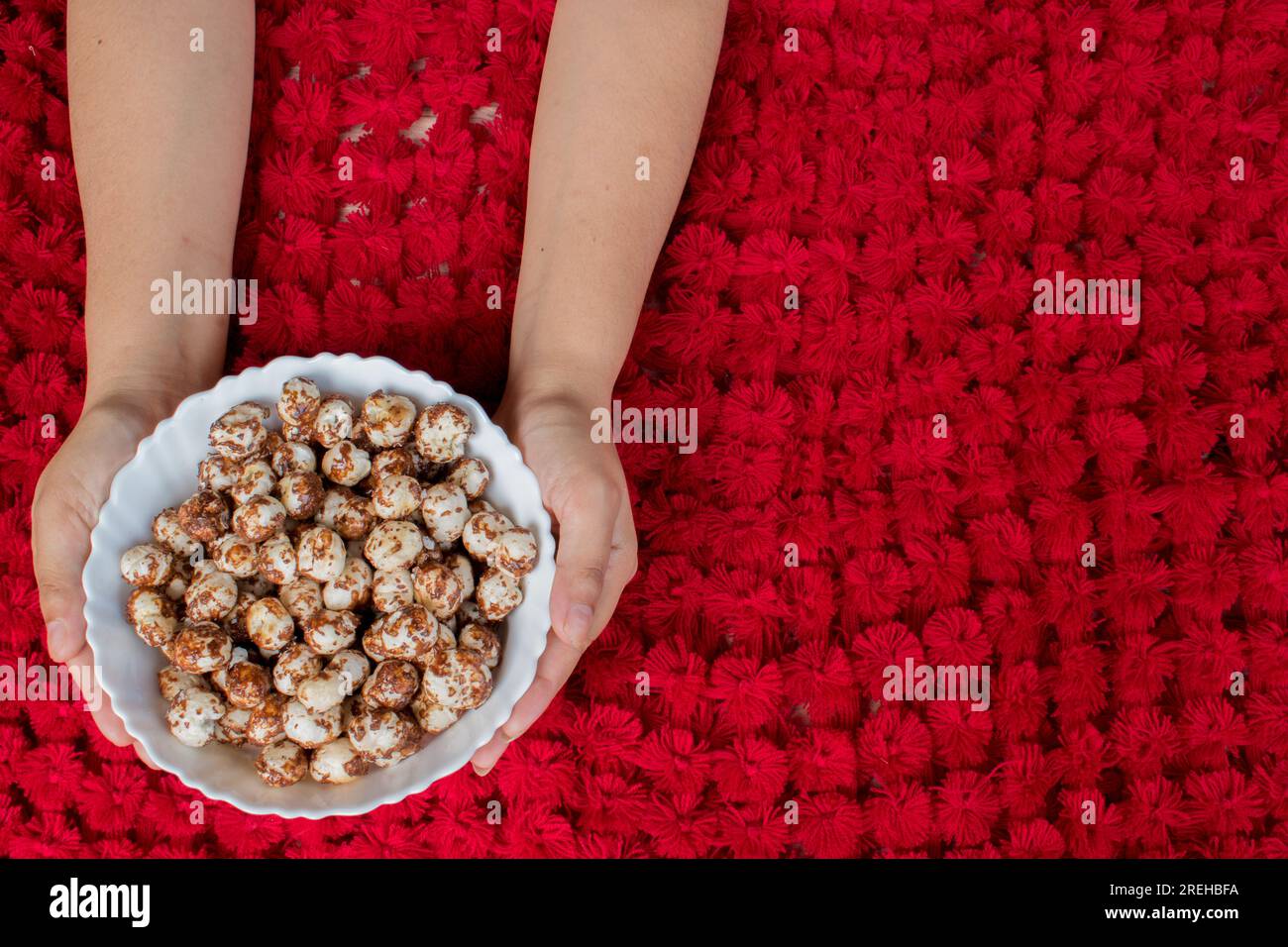 Hand holding white bowl having healthy Chocolate and jaggery coated makhana in beautiful red background. copyspace Stock Photo