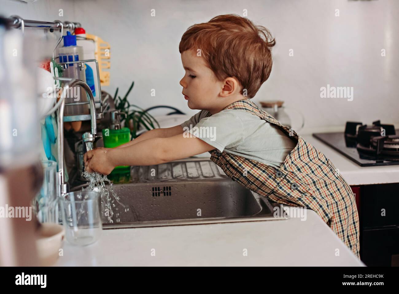 The boy washes his hands in the kitchen. Stock Photo