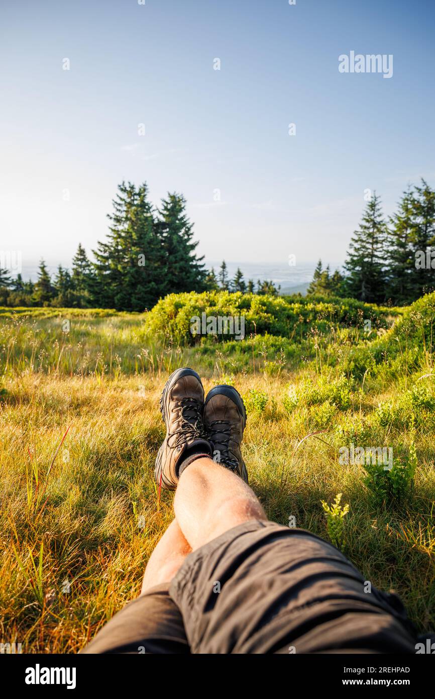 Relaxation in mountain forest during trekking. Crossed male legs with leather hiking boots Stock Photo