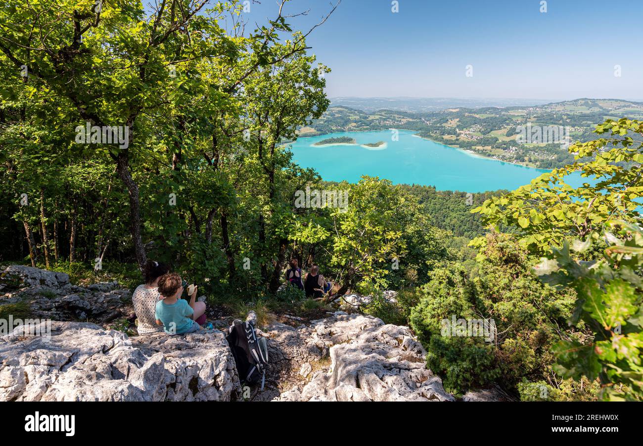 Hikers having lunch on rocks, contemplating the Lac d'Aiguebelette from a view point, a natural lake know for its blue-green colour. Stock Photo