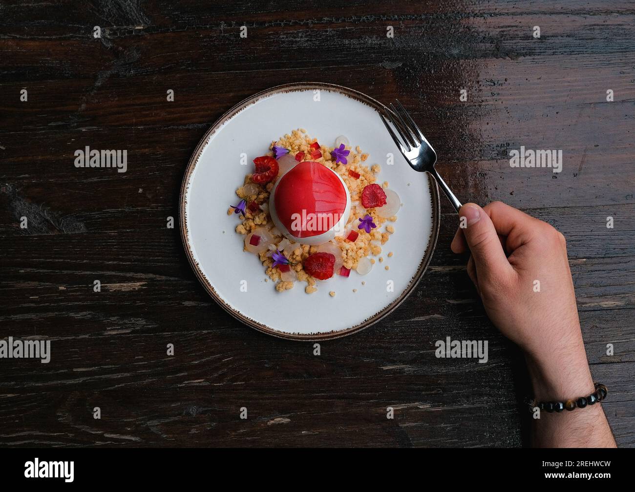 Creative Raspberry dessert plated on a white plate, with crunchy elements and a fork holding hand. Stock Photo