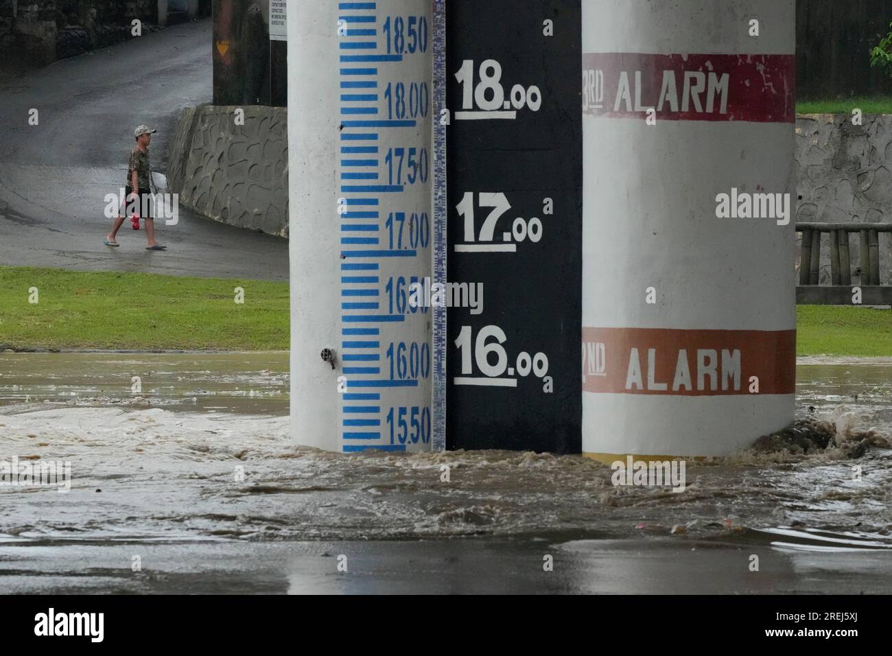 A man walks near a flood alert marker along a swollen river due to ...