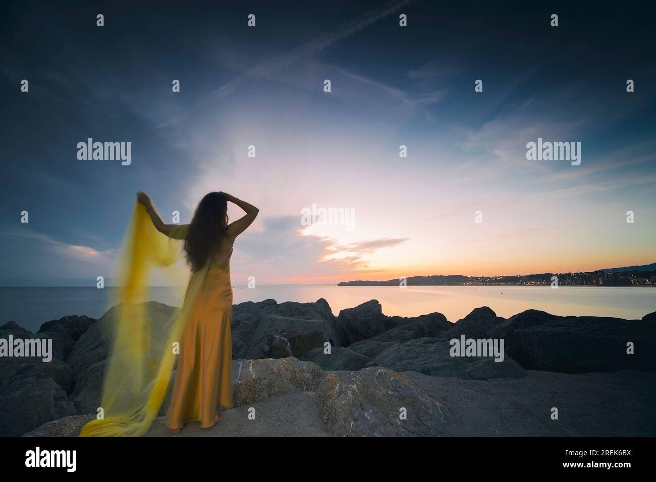 woman in a yellow dress and cape observing a magnificent sunrise on the French Basque coast I Stock Photo